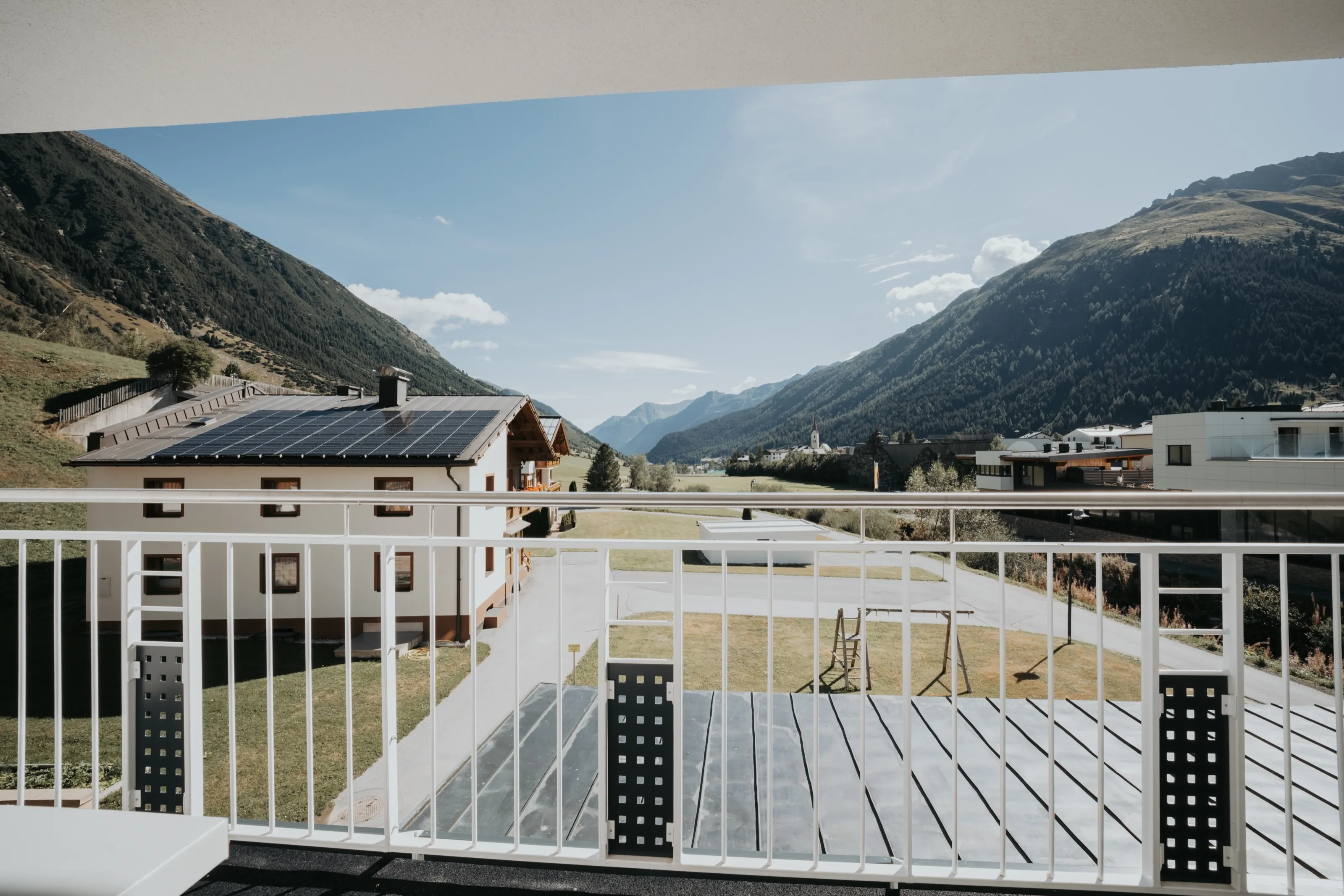 Blick von einem Balkon des Hauses über Wiesen und Nachbarhäuser bis zum Kirchturm von Galtür.