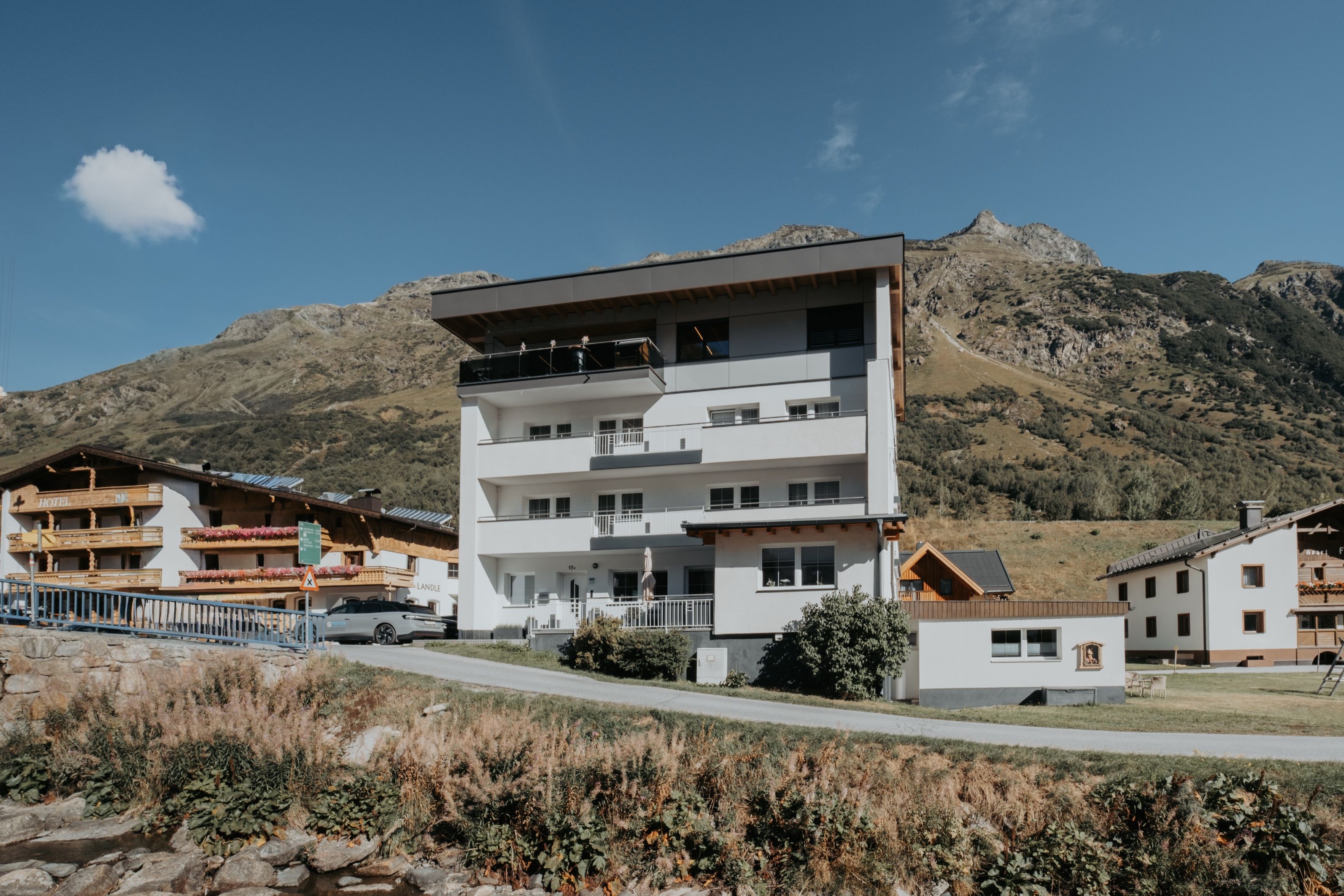 Das Haus Gorfenspitze im Sommer von außen: das ganze Haus mit Balkonen, davor eine Wiese, dahinter der Berghang über Galtür.