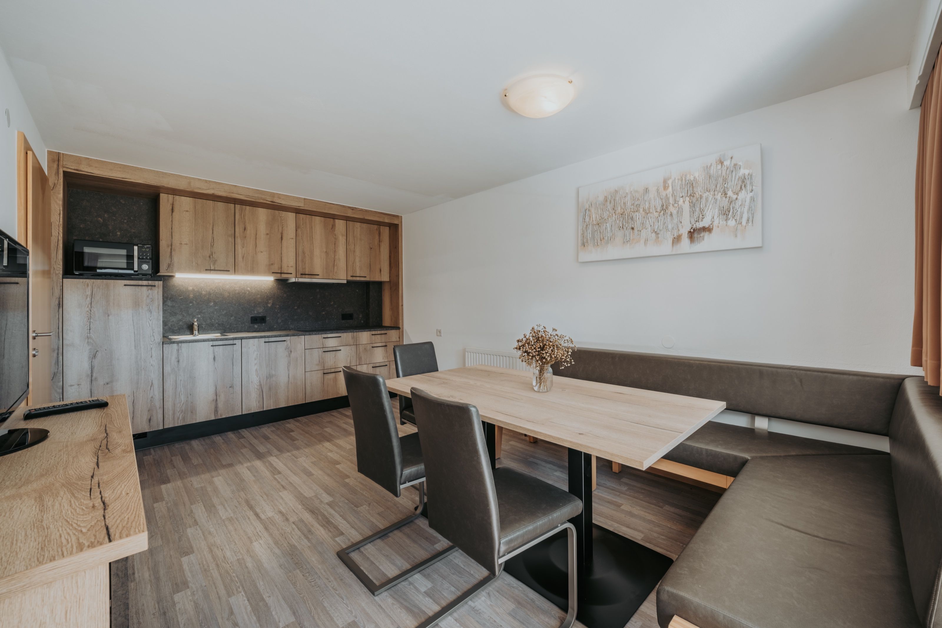 Wohnküche einer Ferienwohnung: Küchenzeile in Eiche mit dunkler Steinrückwand, davor der Esstisch mit Sitzbank.