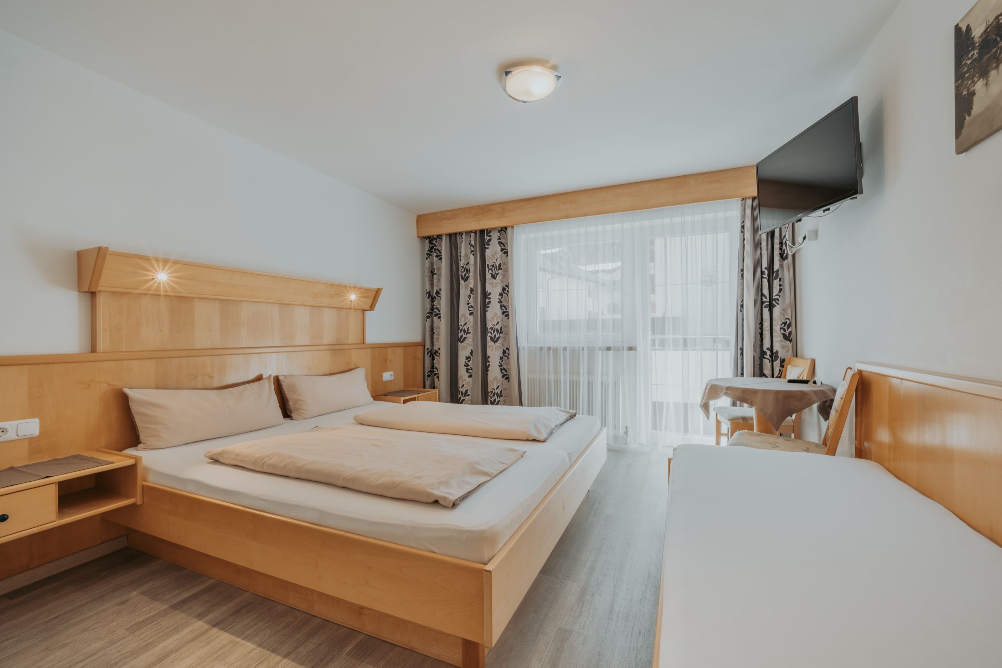 Der Schlafraum der Ferienwohnung für 4 bis 6 Personen in voller Breite: Doppelbett und Zusatzbett in hellem Holz, dazwischen die Balkontür nach Süden.