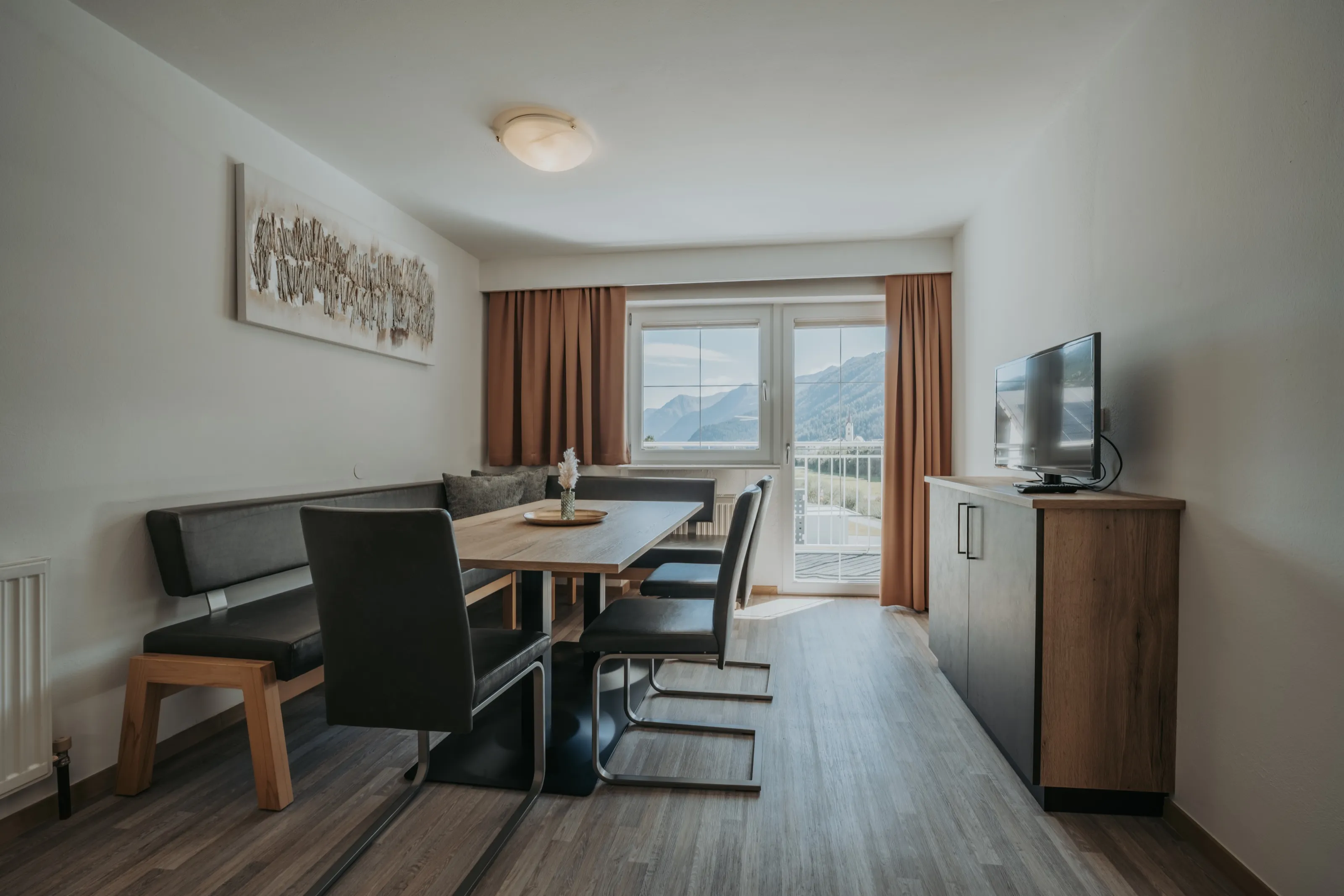 Wohnraum mit Esstisch, Sitzbank und Balkontür mit Blick auf die Berge.