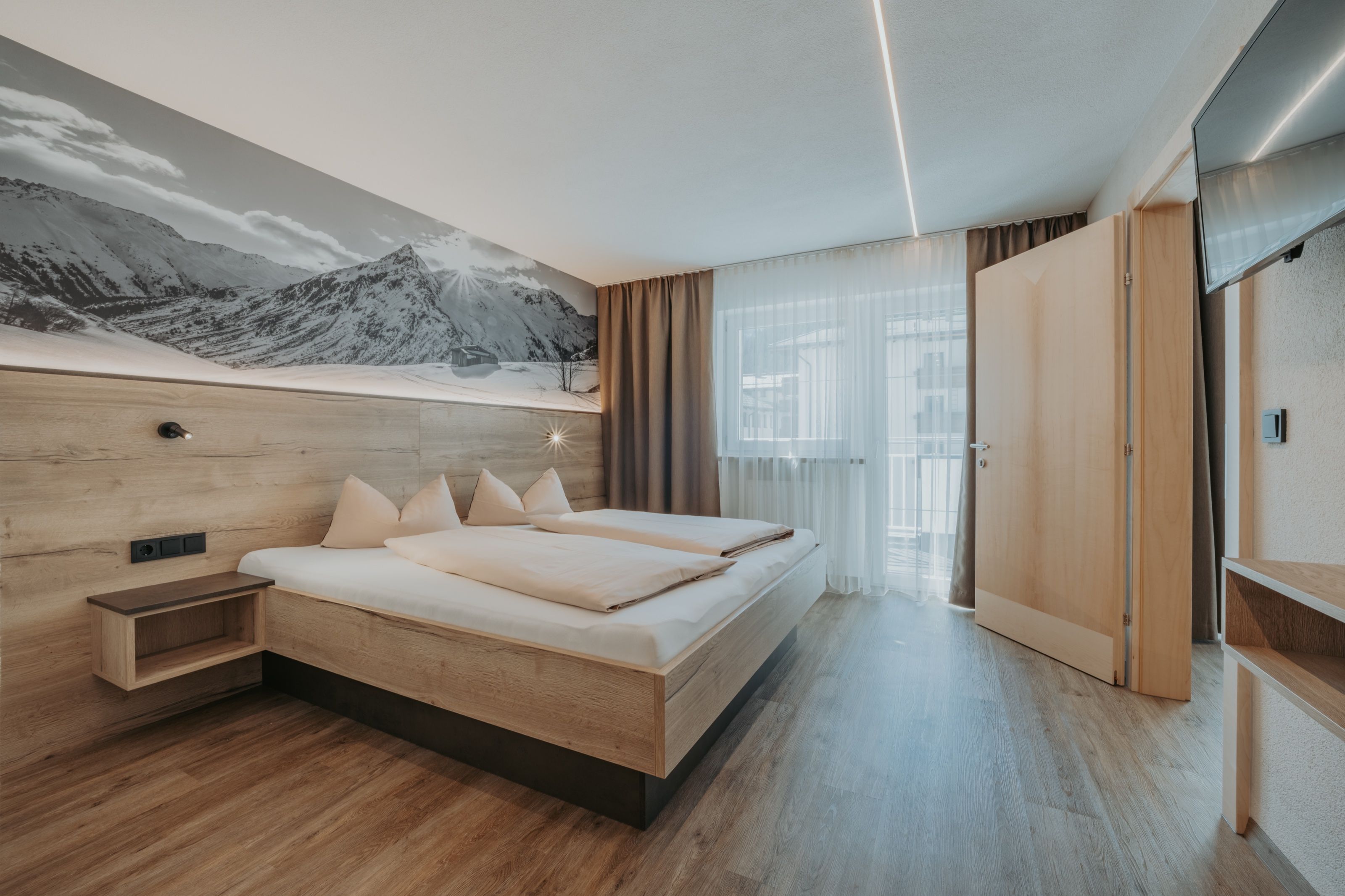 Der Schlafraum der Wohnung für 2 bis 4 Personen: Doppelbett vor einer großformatigen Bergaufnahme, links die Tür zum Balkon.